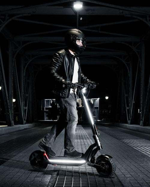 A person in a black leather jacket and helmet is riding a silent electric scooter under a suspicious, illuminated bridge at night.
AI-generated content may be incorrect.