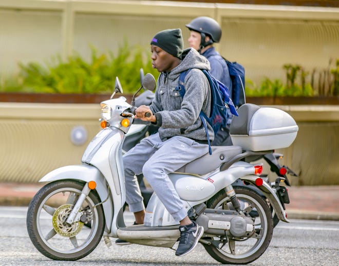 A person rides a scooter with a large, black backpack while wearing a black jacket and black sunglasses.
AI-generated content may be incorrect.