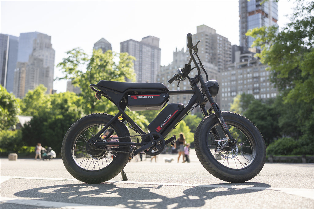 The image shows a black XO/DVN electric scooter parked on a paved street, with a city skyline and green trees in the background.
AI-generated content may be incorrect.