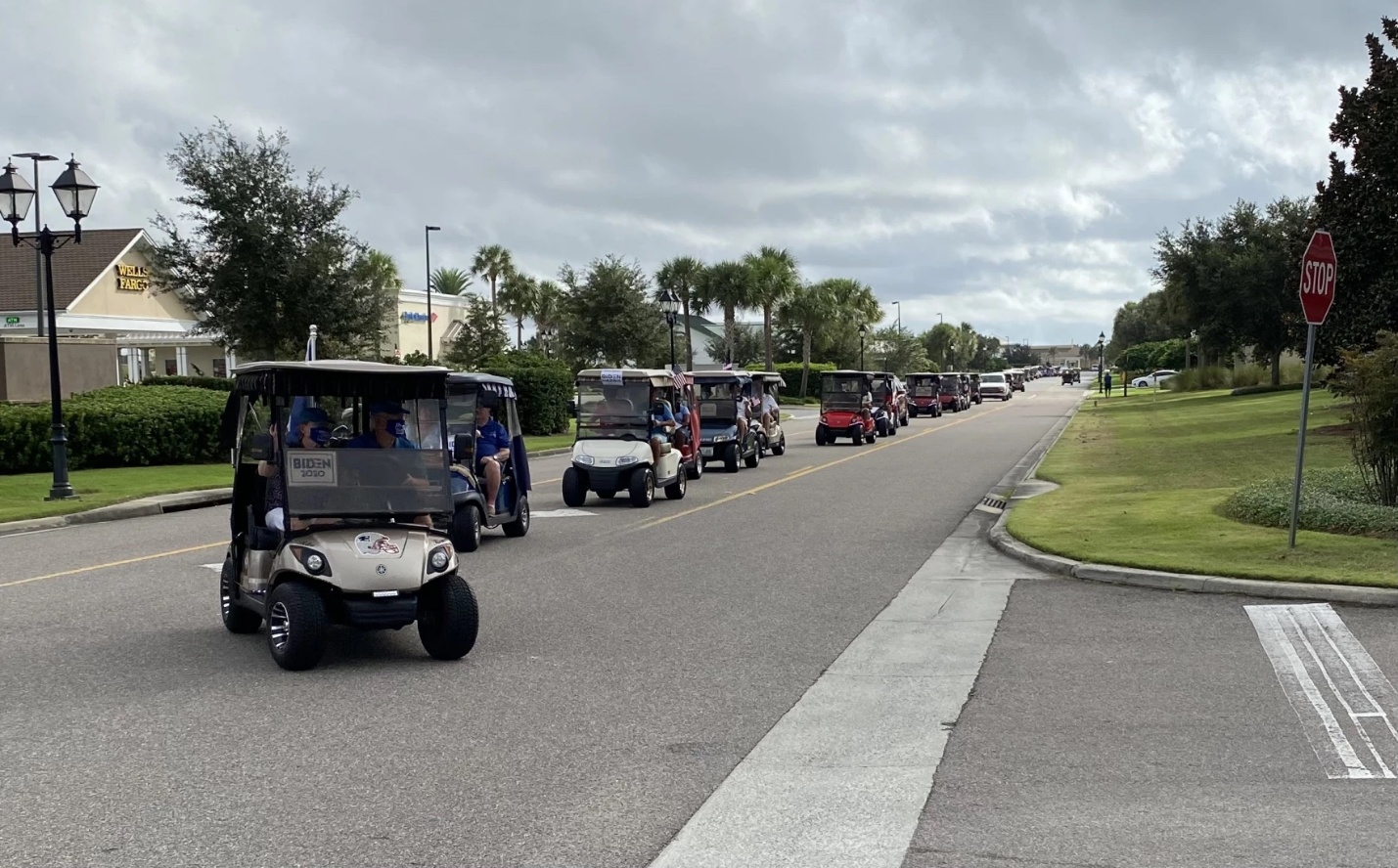 The image shows a street lined with golf carts parked along a grassy median, under a cloudy sky, with buildings and trees in the background.
AI-generated content may be incorrect.